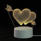 3D LED Lamp featuring a double heart design pierced by an arrow with a golden-yellow optical illusion effect on a white round base