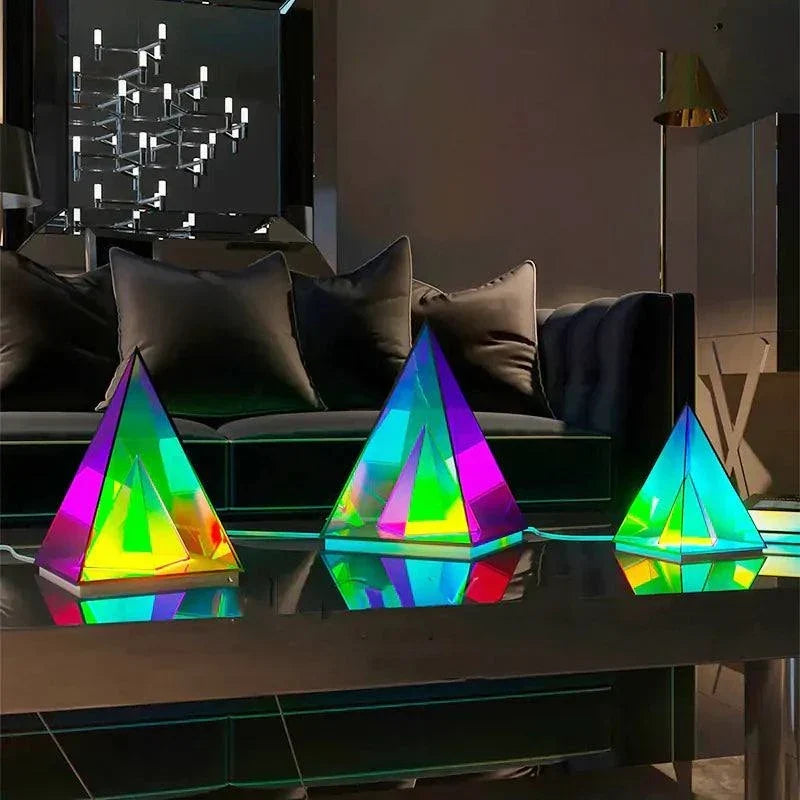 Aura Pyramid Lamp set with three pyramid-shaped acrylic lamps in vibrant rainbow colors on a reflective surface