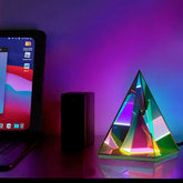 Aura Pyramid Lamp with a translucent triangular design emitting a vibrant rainbow ambient glow on a table