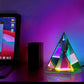 Aura Pyramid Lamp with a translucent triangular design emitting a vibrant rainbow ambient glow on a table