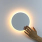 Circular Wall Light with a white circular metal and acrylic design featuring soft warm backlighting and touch-activated control.