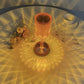 Cristal Lamp with a faceted amber glass body creating intricate light patterns on a white surface, beside dried flowers and a cup