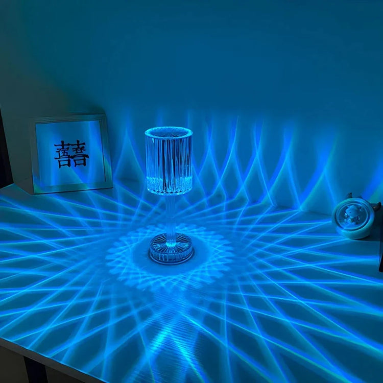 Cristal Lamp with clear faceted glass surface emitting intricate blue light patterns creating a shimmering effect on the table