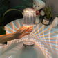 Cristal Lamp with clear faceted glass design creating colorful light reflections, held by a hand above a white surface