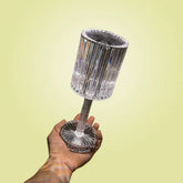 Cristal Lamp with clear faceted glass body and base held in hand, showcasing its compact, decorative design