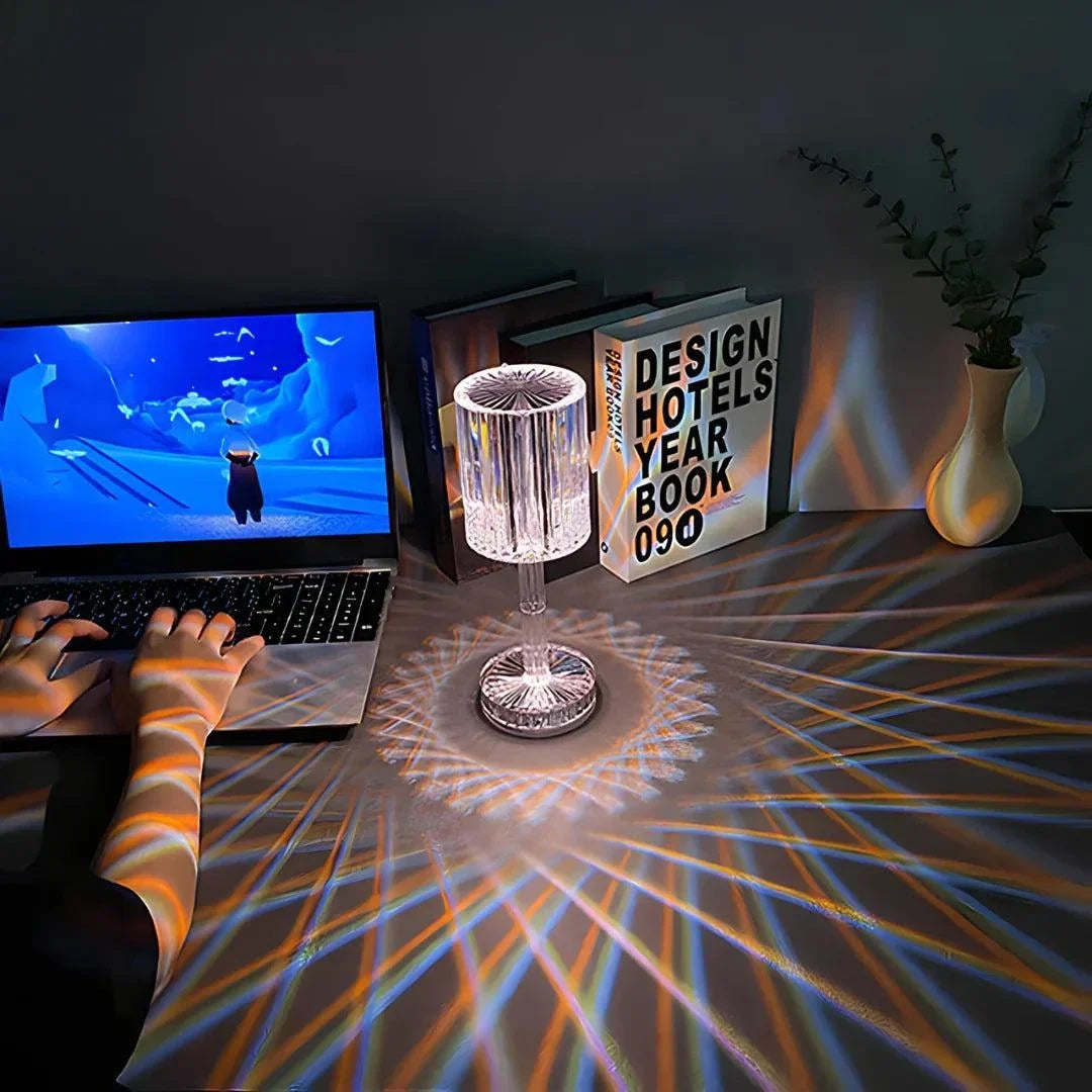 Cristal Lamp with clear faceted glass shade casting intricate light patterns on a wooden table beside books and a laptop