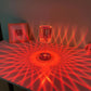 Cristal Lamp with clear cylindrical glass body emitting intricate red light patterns on a surface, creating a radiant decorative effect