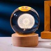 Crystal Night Ball glass sphere with a glowing white dandelion design on a natural wood base