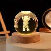 Crystal Night Ball glass globe with a glowing astronaut figure, set on a natural wood base with a round design
