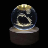 Crystal Night Ball, clear glass sphere with engraved leaping dolphins, stars and moon on a dark wood base