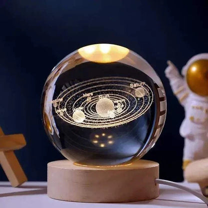 Crystal Night Ball, transparent glass globe with engraved solar system design on a natural wood base
