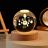 Crystal Night Ball glass sphere with etched solar system design, displayed on a natural wood round base