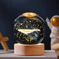 Crystal Night Ball, a black glass orb with glowing stars and whale design on a natural wood base