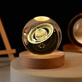 Crystal Night Ball featuring a clear glass planet sphere with Saturn-style rings on a natural wood base, softly glowing