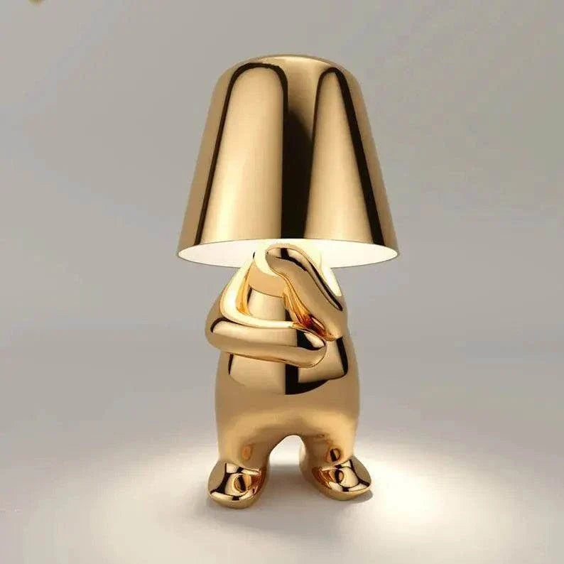 Impression LED Lamp in shiny gold metallic finish with a playful humanoid figure base holding up a smooth lampshade