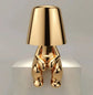 Impression LED Lamp with shiny gold metallic finish shaped like a sitting figure holding the lampshade, sleek and modern design