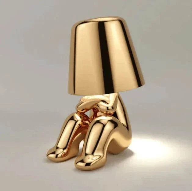 Impression LED Lamp in shiny gold finish shaped like a sitting figure with a lampshade for the head emitting a soft white light
