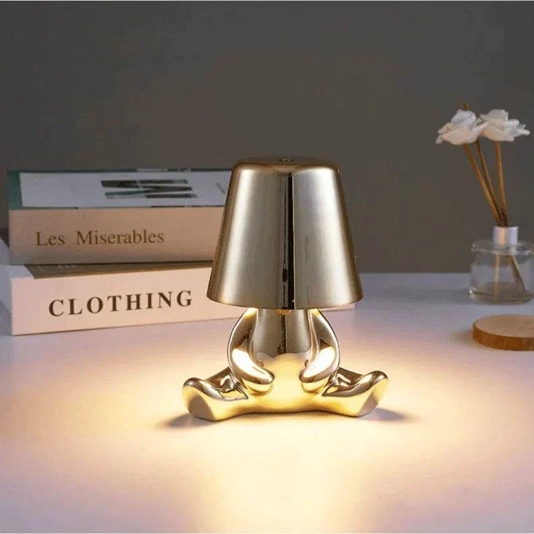 Impression LED Lamp in metallic gold with a unique human figure base and smooth lampshade providing warm, soft light