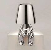 Impression LED Lamp with a modern shiny silver metallic finish shaped like a sitting human figure holding the lampshade