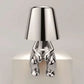 Impression LED Lamp with a modern shiny silver metallic finish shaped like a sitting human figure holding the lampshade