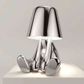 Impression LED Lamp with shiny silver chrome finish featuring a modern, abstract design resembling a seated figure with a reflective lampshade