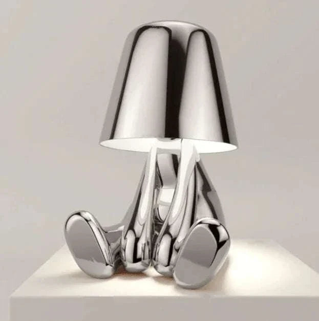 Impression LED Lamp with shiny silver chrome finish featuring a modern, abstract design resembling a seated figure with a reflective lampshade