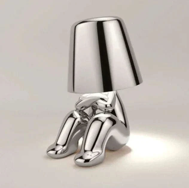 Impression LED Lamp with shiny silver finish featuring a seated humanoid figure design and cone-shaped lampshade