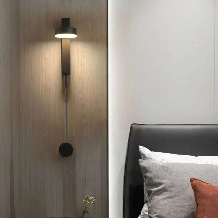 LED indoor Wall Lamps with black metal body and cylindrical shade mounted on a wooden wall beside a bed with cushions