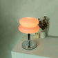 Macaron LED Lamp with a glowing peach macaron-shaped shade, chrome stem, and round mirrored base
