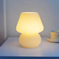 Mushroom LED Lamp with a warm yellow glass body and dome-shaped shade emitting soft ambient light on a white surface