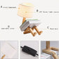 Robot Table Lamp with white cloth lampshade, wooden base shaped like a figure holding a book, and adjustable joint.