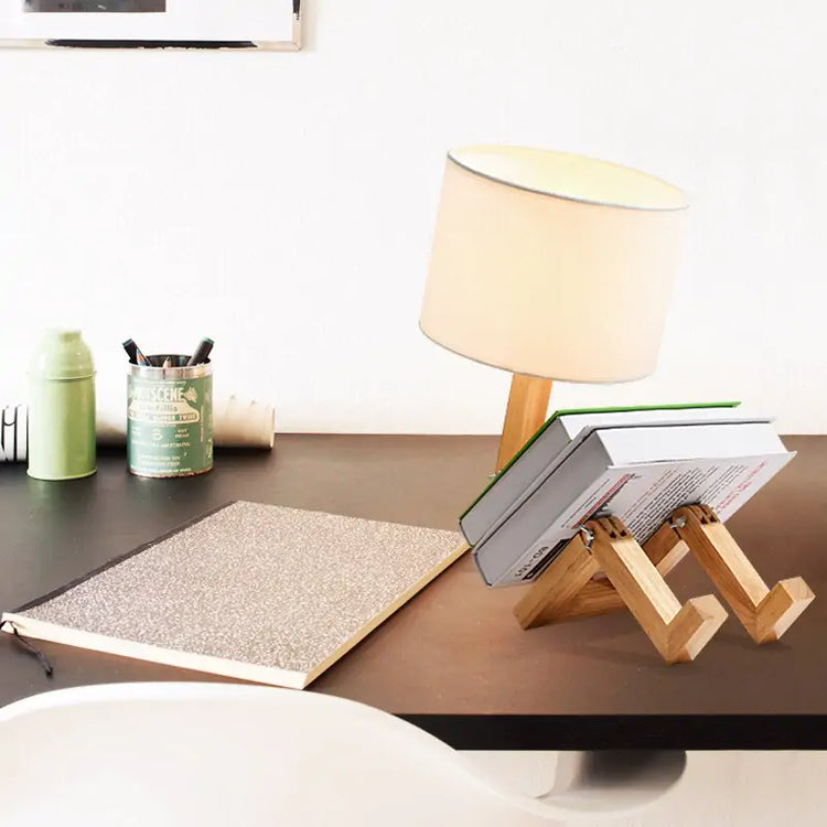 Robot Table Lamp with white fabric lampshade and wooden base doubling as a book holder on a desk surface.