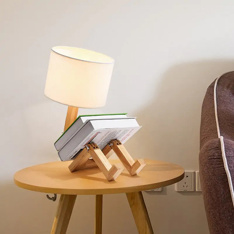 Robot Table Lamp with a white fabric shade and wooden base designed to hold books, featuring a playful robot shape.
