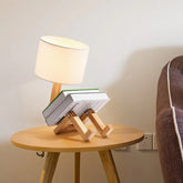 Robot Table Lamp with a white fabric shade and wooden base designed to hold books, featuring a playful robot shape.