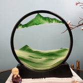 Sand Frame with black circular acrylic frame displaying layered green and white sand forming mountain and landscape patterns