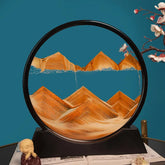 Sand Frame with black circular acrylic frame containing flowing orange sand forming mountain patterns against a blue background