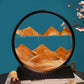 Sand Frame with black circular acrylic frame containing flowing orange sand forming mountain patterns against a blue background