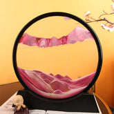 Sand Frame with black circular acrylic frame containing vibrant pink and white sand forming mountain-like patterns on a clear enclosed display