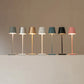Cordless lamp set featuring slender metal stems and fabric shades in grey, silver, gold, white, teal, black, and pink colors.