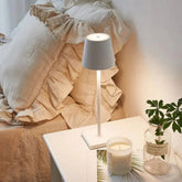 Cordless lamp with a sleek white metal frame and minimalist design, emitting warm light for cozy indoor ambiance.
