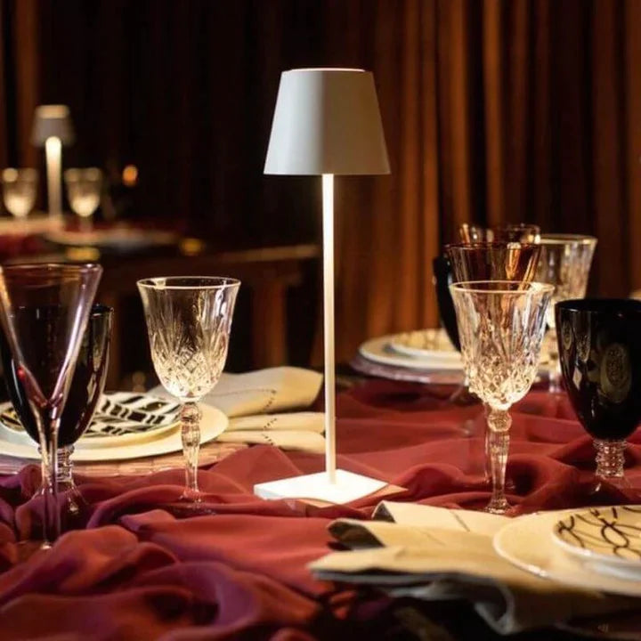 Cordless lamp with a sleek white metal base and shade, providing warm ambient lighting on a dining table.