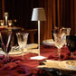 Cordless lamp with a sleek white metal base and shade, providing warm ambient lighting on a dining table.