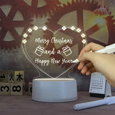 LED Note Board with clear acrylic heart-shaped panel displaying festive handwritten message with decorative icons, glowing warmly on white base