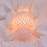 Mushroom LED Lamp with hand-blown clear glass and white spiral pattern emitting warm light on soft fabric