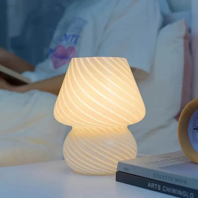 Mushroom LED Lamp made of white glass with diagonal striped pattern, emitting warm light on a bedside table