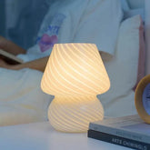 Mushroom LED Lamp made of white glass with diagonal striped pattern, emitting warm light on a bedside table