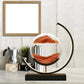 Sandscape Lamp with clear glass containment vessel filled with shifting red and white sand on black rectangular base and curved gold frame